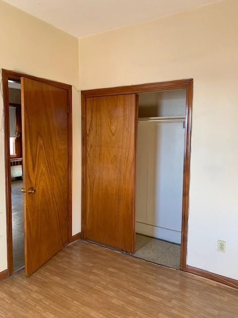 unfurnished bedroom with radiator heating unit, a closet, and light wood-type flooring