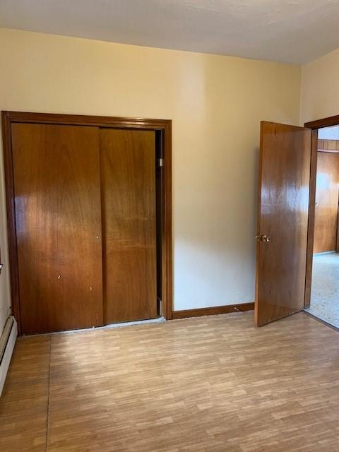 unfurnished bedroom featuring a baseboard radiator, light hardwood / wood-style floors, and a closet