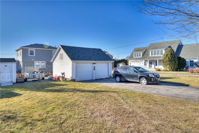 exterior space with roof with shingles, a detached garage, a front lawn, and an outdoor structure