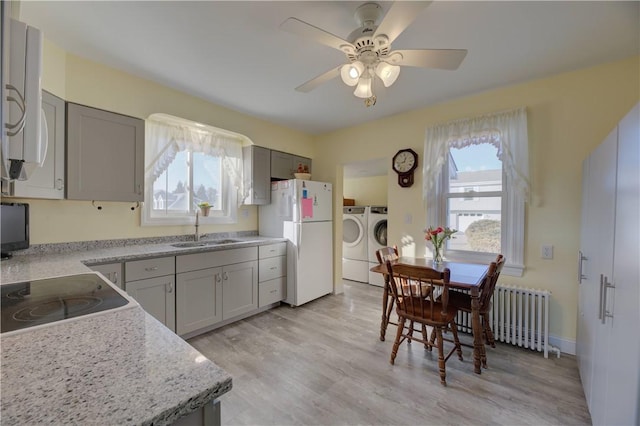 kitchen with a sink, light wood-style floors, freestanding refrigerator, radiator heating unit, and washing machine and clothes dryer