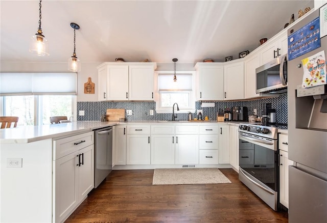 kitchen with appliances with stainless steel finishes, decorative light fixtures, white cabinets, kitchen peninsula, and a healthy amount of sunlight