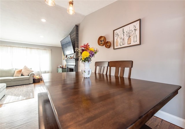 dining space with wood-type flooring, lofted ceiling, and a fireplace