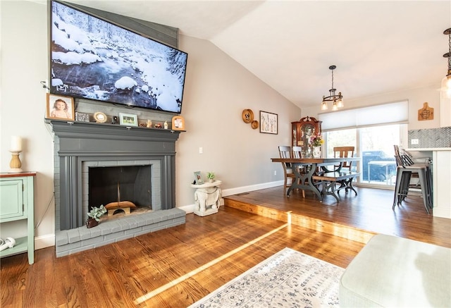 living room featuring lofted ceiling, a brick fireplace, a chandelier, and wood-type flooring