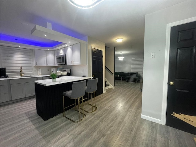 kitchen with sink, a breakfast bar area, gray cabinetry, stainless steel appliances, and hardwood / wood-style floors