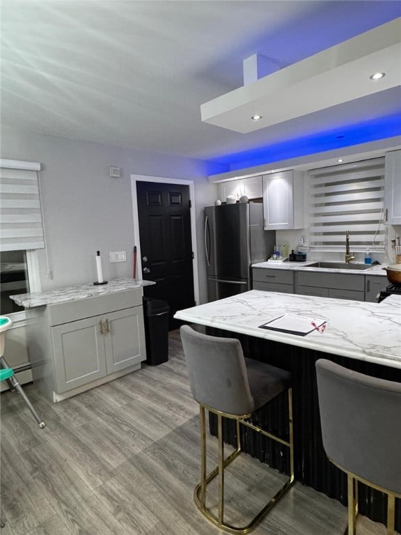 kitchen with a kitchen bar, sink, light wood-type flooring, stainless steel refrigerator, and gray cabinets