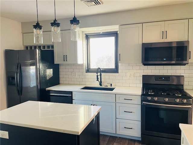 kitchen with sink, hanging light fixtures, a kitchen island, stainless steel appliances, and white cabinets