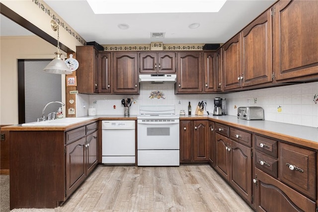 kitchen with sink, white appliances, backsplash, a skylight, and decorative light fixtures