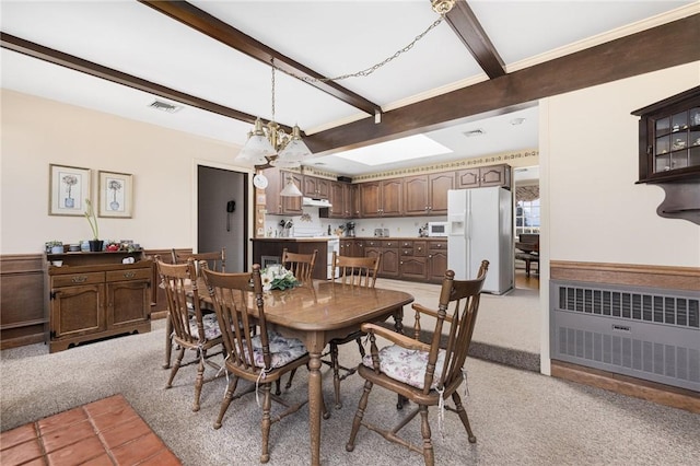 dining area featuring light carpet, a notable chandelier, beam ceiling, and radiator heating unit