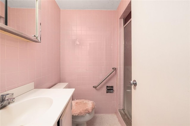 bathroom featuring tile patterned floors, toilet, tile walls, vanity, and a shower with door