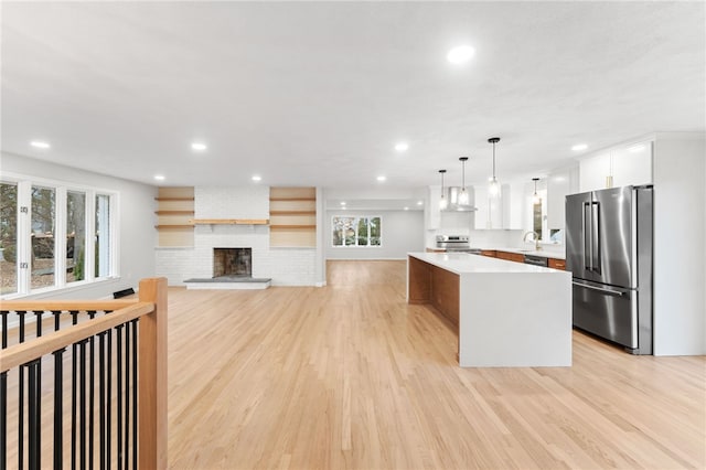 kitchen featuring a kitchen island, decorative light fixtures, white cabinetry, stainless steel appliances, and wall chimney exhaust hood