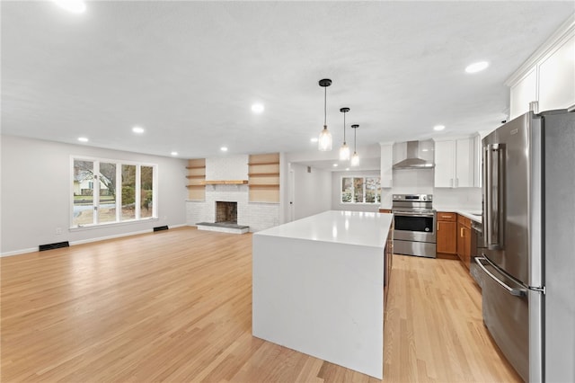 kitchen featuring white cabinetry, hanging light fixtures, a kitchen island, stainless steel appliances, and wall chimney range hood