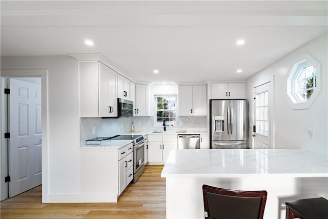 kitchen featuring a breakfast bar area, stainless steel appliances, light stone counters, white cabinets, and light wood-type flooring