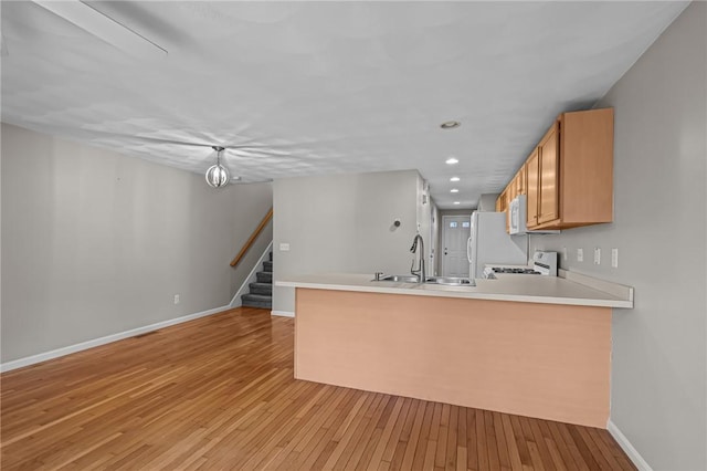 kitchen with light hardwood / wood-style floors, white appliances, kitchen peninsula, and sink