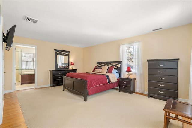 bedroom featuring ensuite bathroom, multiple windows, and light hardwood / wood-style flooring