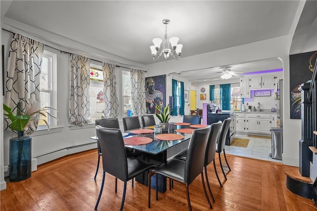 dining space with a baseboard radiator, ceiling fan with notable chandelier, a wealth of natural light, and light hardwood / wood-style flooring