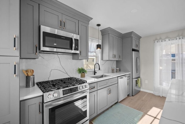 kitchen with sink, gray cabinetry, light hardwood / wood-style flooring, hanging light fixtures, and appliances with stainless steel finishes