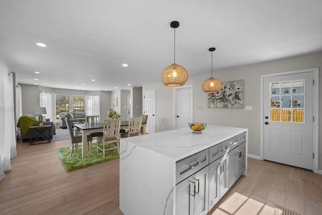 kitchen featuring decorative light fixtures, gray cabinetry, a center island, light hardwood / wood-style floors, and light stone countertops