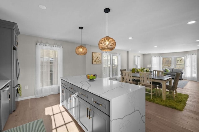 kitchen featuring gray cabinets, hanging light fixtures, light stone countertops, light hardwood / wood-style floors, and a kitchen island