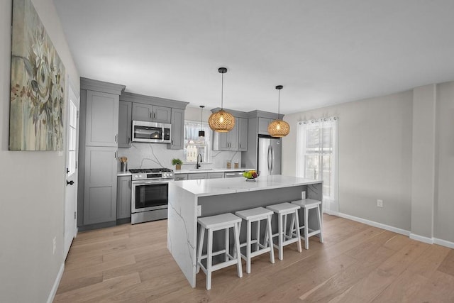 kitchen with appliances with stainless steel finishes, sink, gray cabinetry, a center island, and light stone counters