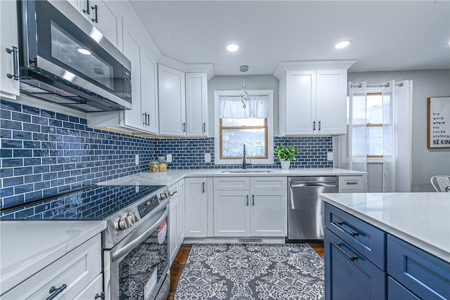 kitchen with sink, appliances with stainless steel finishes, white cabinetry, hanging light fixtures, and plenty of natural light