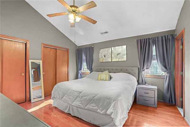 bedroom featuring multiple closets, vaulted ceiling, ceiling fan, and light hardwood / wood-style floors