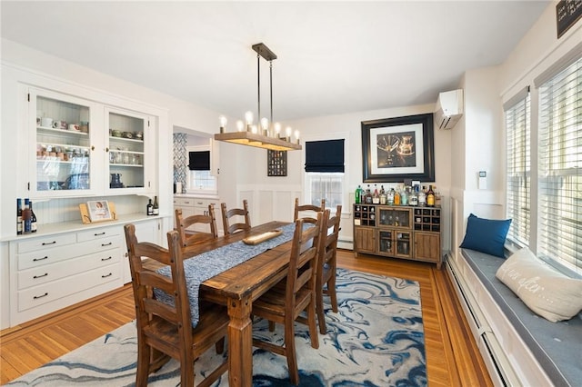 dining area with a baseboard radiator, light wood-type flooring, an inviting chandelier, and a wall unit AC