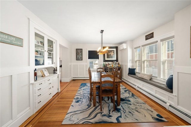 dining room with light wood-type flooring, a wall mounted air conditioner, a notable chandelier, and baseboard heating