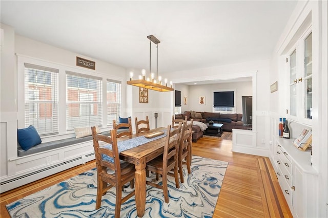 dining space with a baseboard radiator, a notable chandelier, and light wood-type flooring