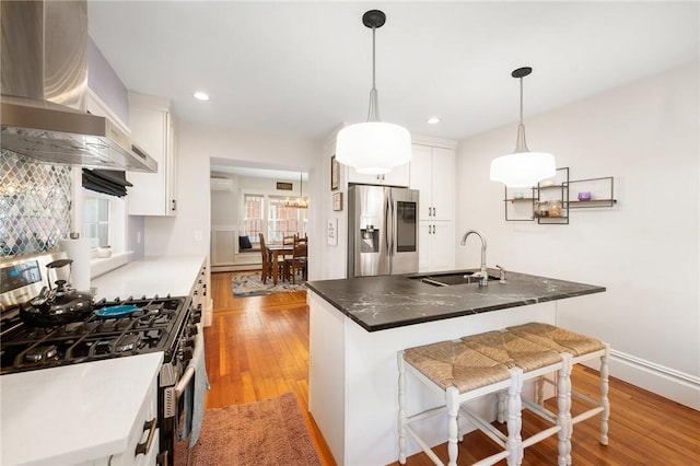 kitchen featuring appliances with stainless steel finishes, decorative light fixtures, sink, white cabinets, and wall chimney exhaust hood