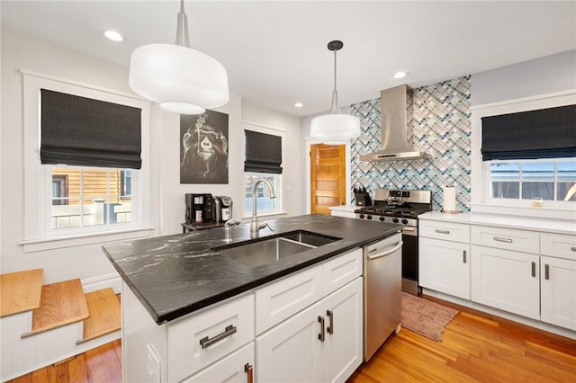 kitchen featuring wall chimney exhaust hood, sink, hanging light fixtures, an island with sink, and stainless steel appliances