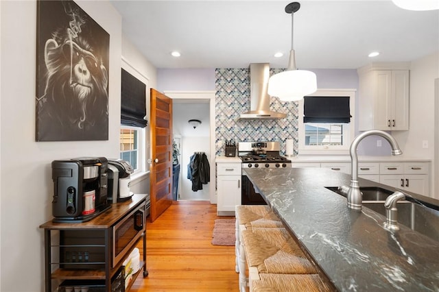 kitchen with hanging light fixtures, white cabinetry, wall chimney exhaust hood, and stainless steel gas stove