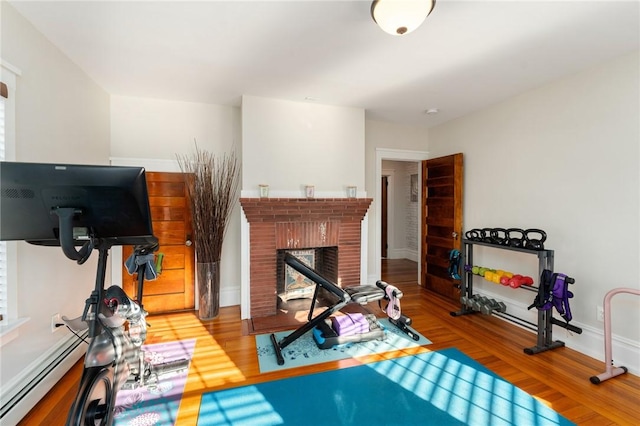 exercise area featuring a baseboard heating unit, hardwood / wood-style flooring, and a fireplace