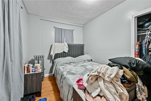 bedroom with radiator, light hardwood / wood-style flooring, and a textured ceiling