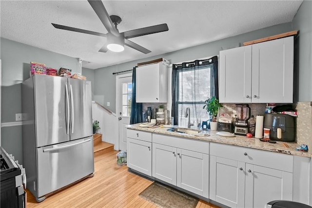 kitchen with sink, tasteful backsplash, light wood-type flooring, stainless steel refrigerator, and white cabinets