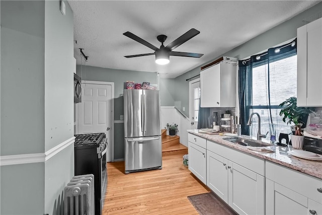 kitchen with radiator heating unit, white cabinetry, sink, light hardwood / wood-style floors, and stainless steel appliances