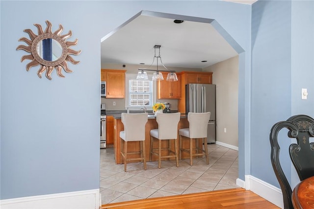 kitchen with light tile patterned flooring, a breakfast bar, a center island, hanging light fixtures, and appliances with stainless steel finishes