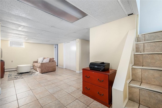 basement featuring a baseboard radiator, a drop ceiling, and light tile patterned floors