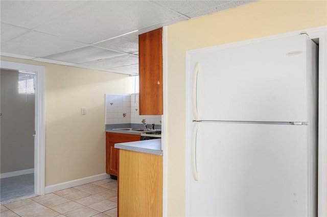 kitchen featuring sink, a paneled ceiling, light tile patterned flooring, decorative backsplash, and white fridge