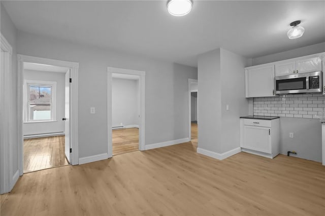 kitchen with a baseboard radiator, white cabinets, light wood-type flooring, and decorative backsplash