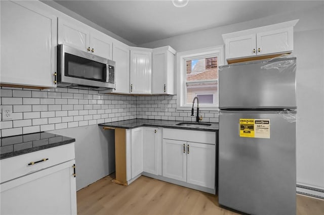 kitchen with sink, appliances with stainless steel finishes, light hardwood / wood-style floors, white cabinets, and decorative backsplash