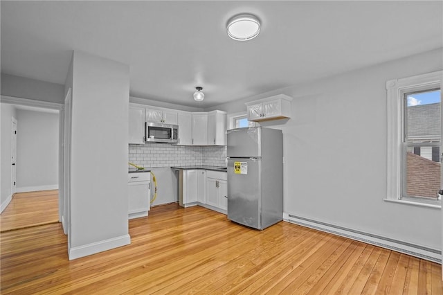 kitchen featuring appliances with stainless steel finishes, white cabinetry, a baseboard radiator, backsplash, and light hardwood / wood-style flooring