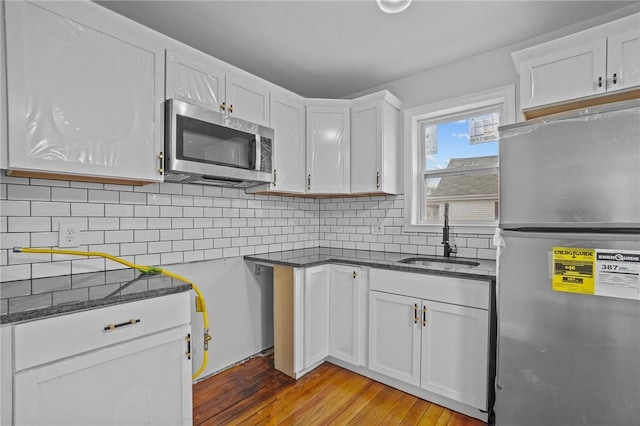 kitchen with appliances with stainless steel finishes, sink, white cabinets, decorative backsplash, and light hardwood / wood-style flooring