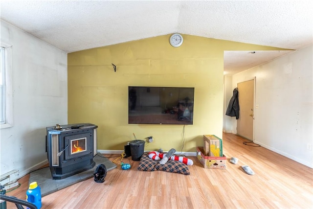 living room featuring hardwood / wood-style flooring, vaulted ceiling, a textured ceiling, and a wood stove