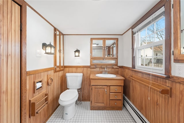 bathroom featuring tile patterned floors, toilet, vanity, wooden walls, and a baseboard heating unit