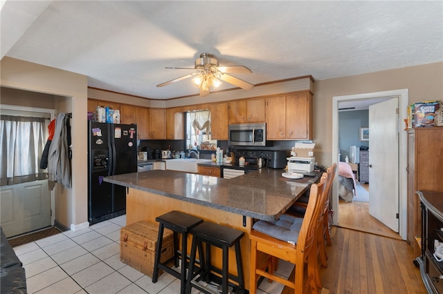 kitchen featuring black appliances, sink, a kitchen breakfast bar, ceiling fan, and kitchen peninsula