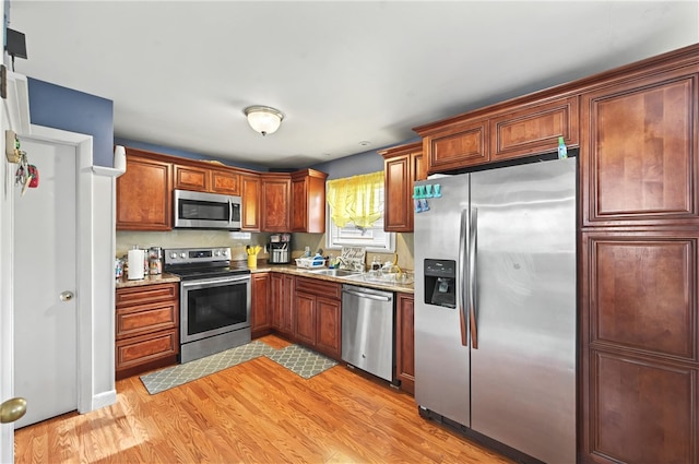 kitchen with stainless steel appliances, sink, light stone counters, and light hardwood / wood-style floors