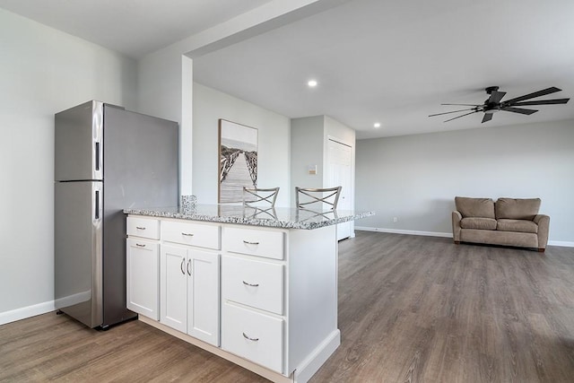 kitchen featuring wood-type flooring, stainless steel fridge, white cabinets, ceiling fan, and light stone countertops