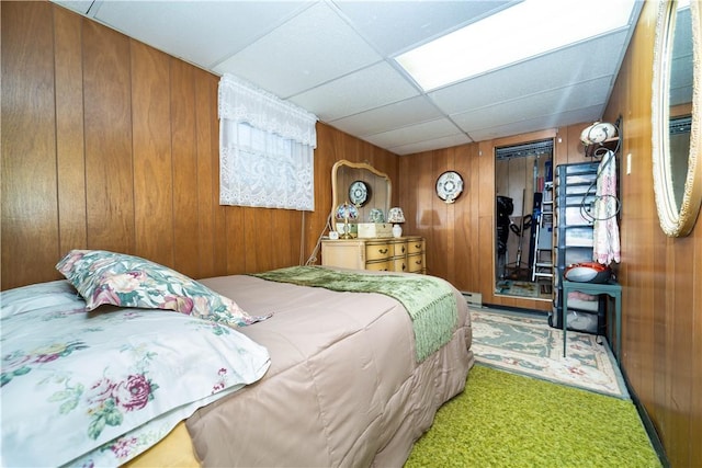 bedroom with a paneled ceiling, wooden walls, and a closet