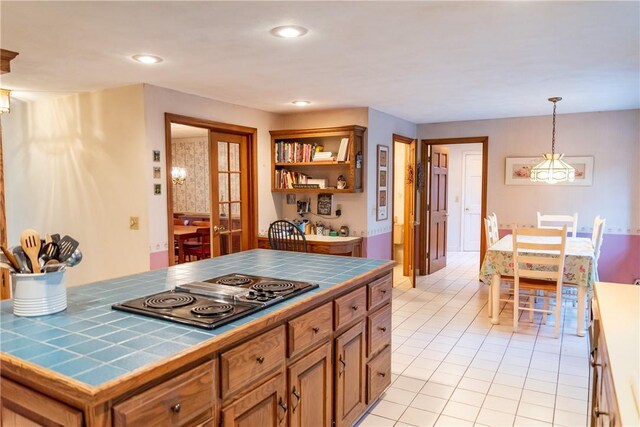 kitchen featuring tile counters, stainless steel gas cooktop, hanging light fixtures, and light tile patterned floors