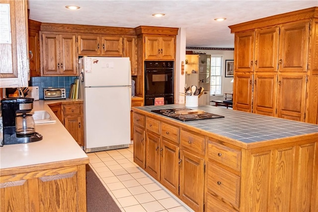 kitchen with light tile patterned floors, tasteful backsplash, black appliances, a kitchen island, and tile countertops